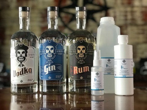 Three bottles labeled Vodka, Gin, and Rum, alongside two smaller bottles and a spray bottle on a wooden surface.