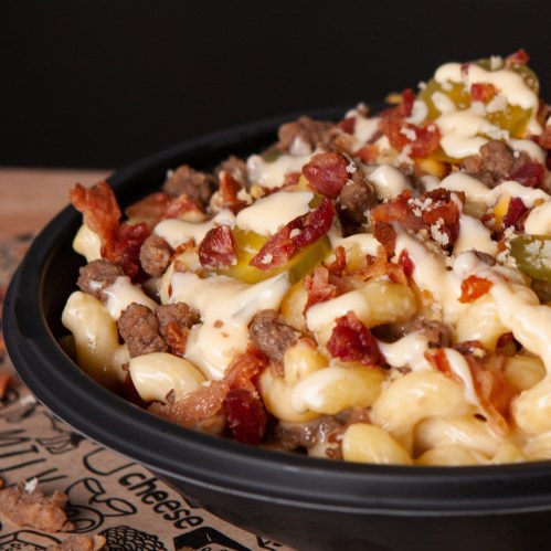 A close-up of a bowl of pasta topped with ground beef, bacon, pickles, and drizzled with creamy sauce.