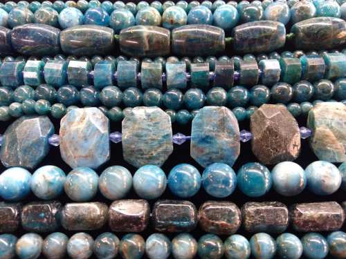 A close-up of various blue gemstones and beads arranged in rows, showcasing different shapes and textures.
