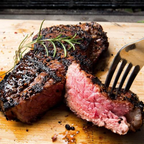A perfectly cooked steak on a wooden cutting board, garnished with rosemary, with a fork piercing into it.