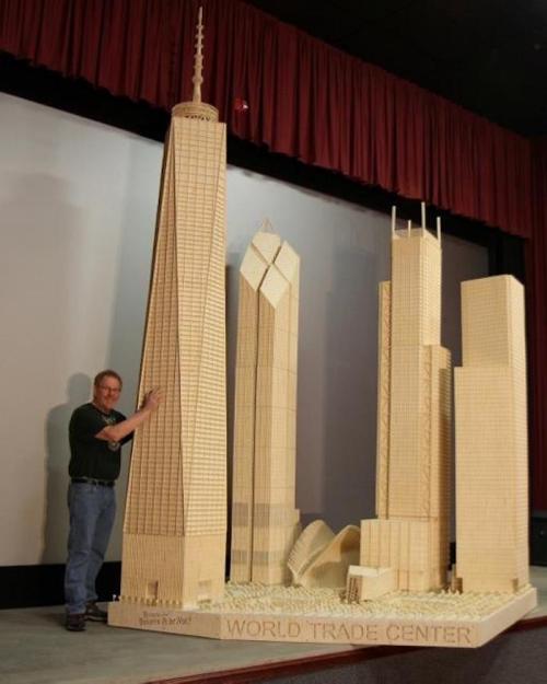 A man stands next to a large wooden model of the World Trade Center and surrounding buildings.