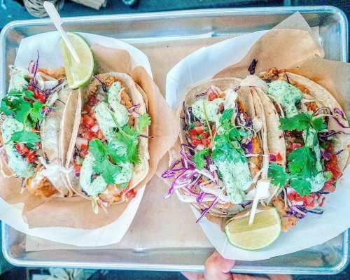A tray of tacos topped with cilantro, pico de gallo, and a creamy sauce, served with lime wedges.