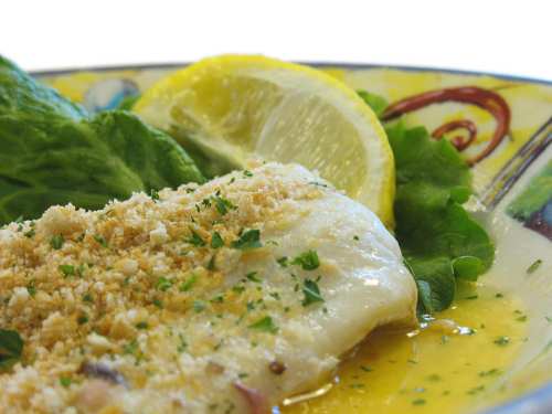 A plate of baked fish topped with breadcrumbs, served with lemon slices and fresh lettuce on a colorful dish.