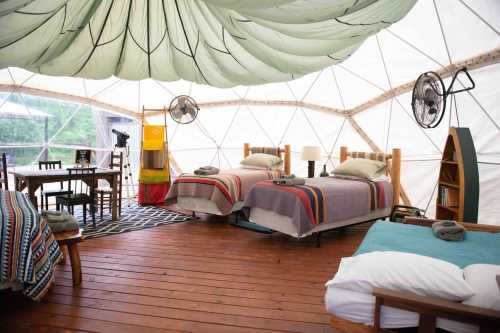 Cozy interior of a geodesic dome with two beds, a dining table, and rustic decor.