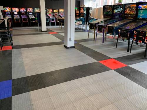 A spacious arcade with colorful pinball machines and a patterned floor in gray, black, and red tiles.