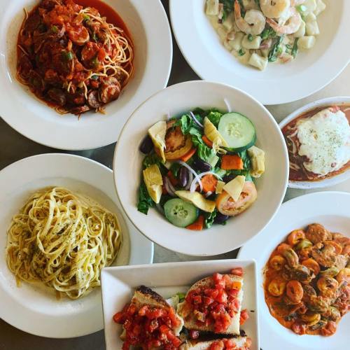 A spread of Italian dishes including pasta, salad, and bruschetta, arranged in white bowls and plates.