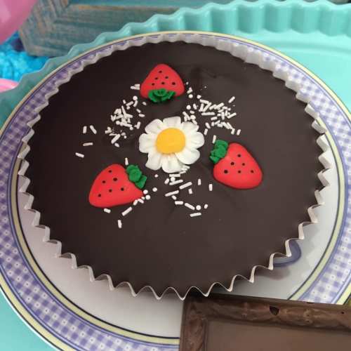 A chocolate pie decorated with strawberries, a daisy, and sprinkles on a blue plate.