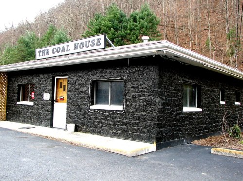 A black stone building with a sign reading "The Coal House," surrounded by trees and a gravel parking area.