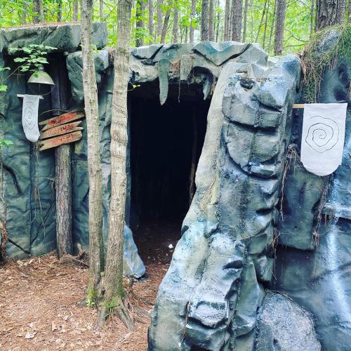A rocky cave entrance surrounded by trees, with wooden signs pointing in different directions.