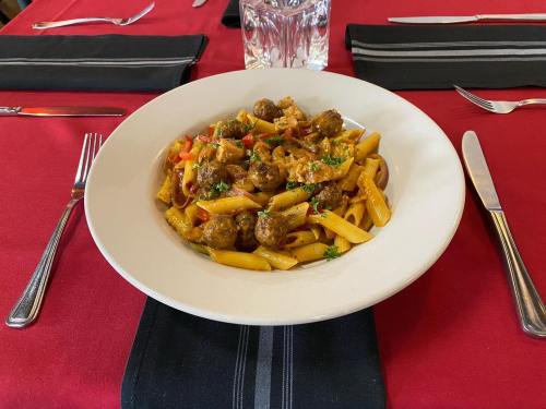 A plate of pasta with meatballs and vegetables, set on a red tablecloth with silverware and a glass in the background.