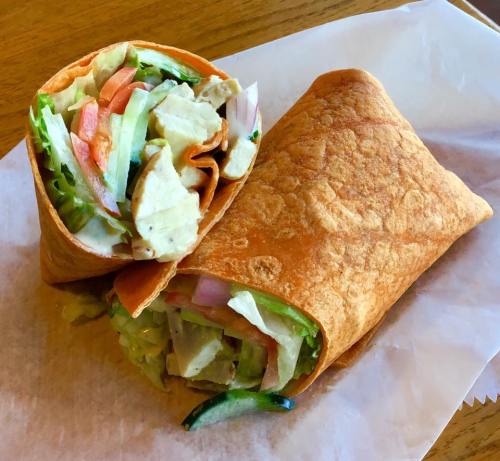 A wrap filled with chicken, lettuce, tomatoes, and cucumbers, resting on a white paper surface.