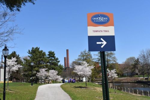 Sign for the Ohio & Erie Canalway Towpath Trail, with cherry blossom trees and a path leading alongside a canal.