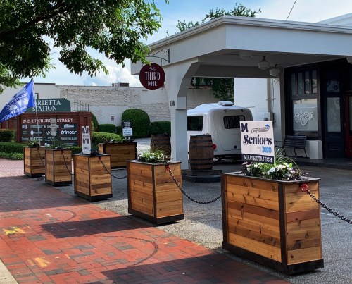 Outdoor view of The Third Door with wooden planters, flowers, and a sign for Marietta High School seniors.