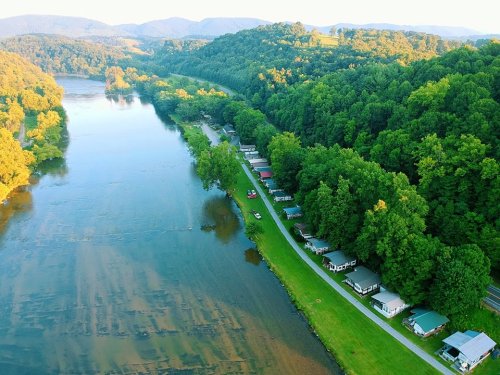 Aerial view of a river bordered by lush greenery and a row of cabins along a winding road.