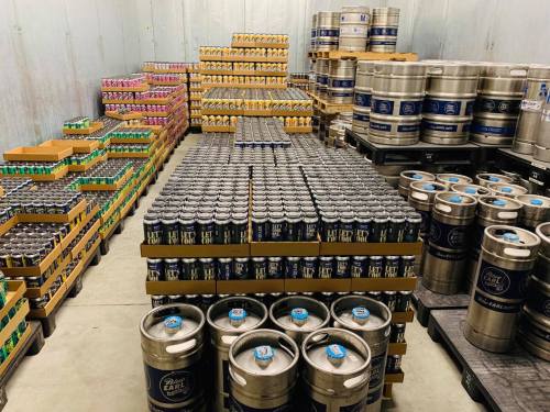 A warehouse filled with stacked cans and kegs of beer, organized in neat rows on pallets.