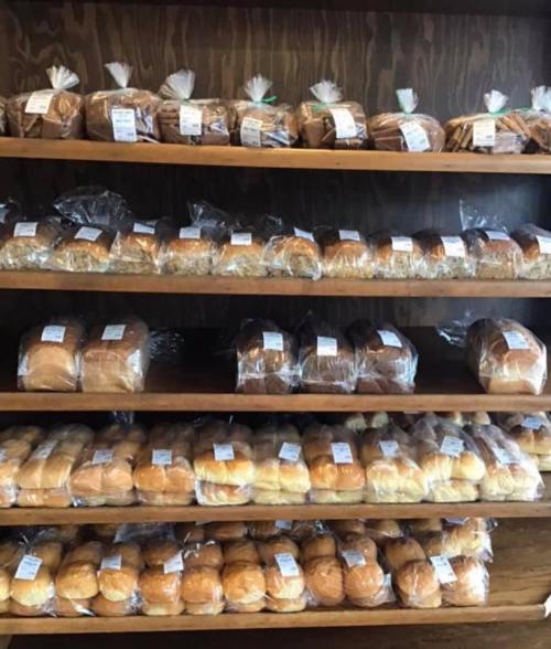 A wooden shelf displaying various types of packaged bread and rolls, neatly arranged in rows.