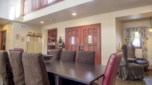 A spacious dining area with a dark table, brown chairs, and a cozy seating nook in a well-lit room.