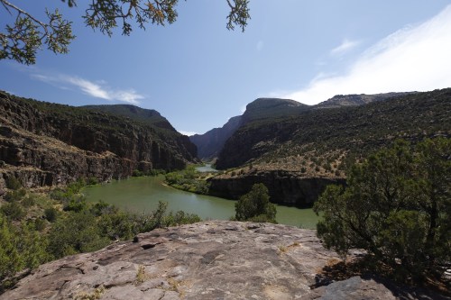 A scenic view of a river winding through rocky cliffs and green hills under a clear blue sky.