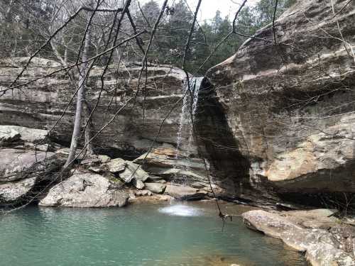 A serene waterfall cascades over rocky cliffs into a tranquil pool, surrounded by trees and natural beauty.