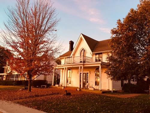 A charming white house with a porch, surrounded by autumn trees and fallen leaves, under a colorful sunset sky.