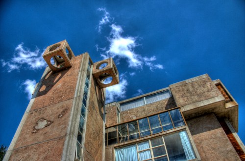 A unique modern building with circular windows and a textured facade, set against a bright blue sky with clouds.