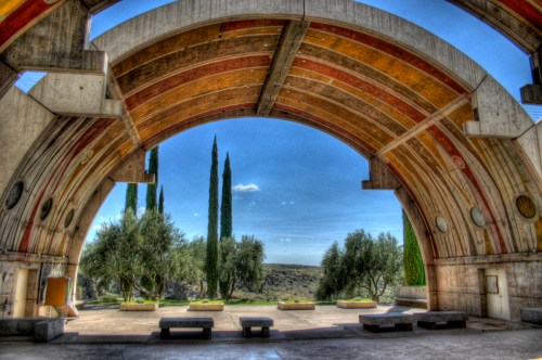 A colorful archway frames a view of cypress trees and olive trees against a blue sky.