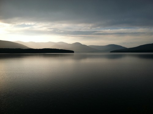 A serene lake reflects mountains under a cloudy sky, creating a tranquil and picturesque landscape.