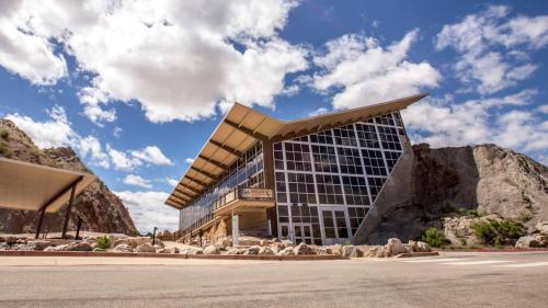 Modern building with large glass windows, set against rocky mountains and a blue sky with fluffy clouds.