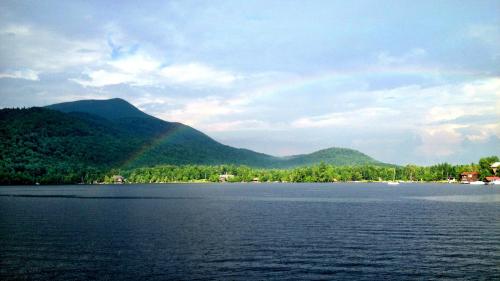 A serene lake scene with green mountains, a rainbow in the sky, and a calm water surface reflecting the landscape.