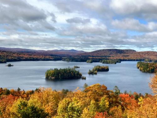 A scenic view of a lake surrounded by colorful autumn foliage and islands, under a partly cloudy sky.
