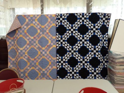 Two colorful quilts displayed side by side: one with a light blue pattern and the other in black and white geometric designs.