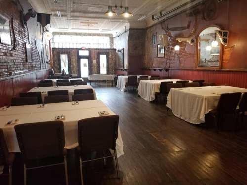 Interior of a restaurant featuring empty tables with white tablecloths, wooden floors, and a welcoming entrance.