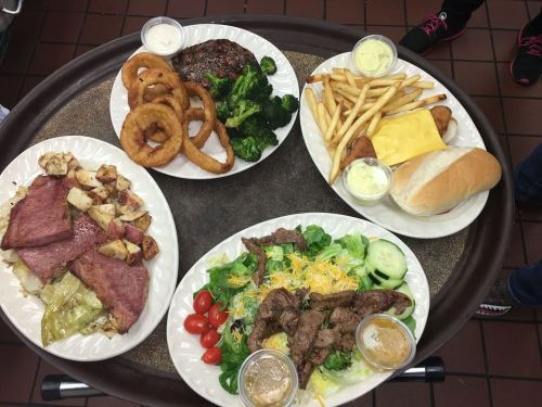 A tray with four plates of food: steak, onion rings, broccoli, fries, ham, cabbage, salad, and a roll with dipping sauces.