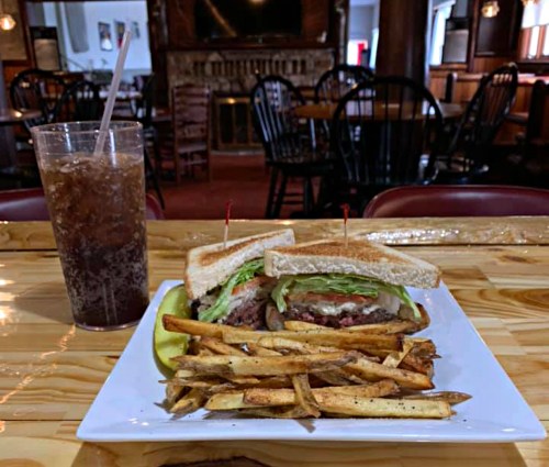A plate with a sandwich and fries, alongside a glass of soda, set in a cozy restaurant interior.