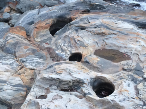 Rocky shoreline with smooth, multicolored stones featuring natural depressions filled with water.