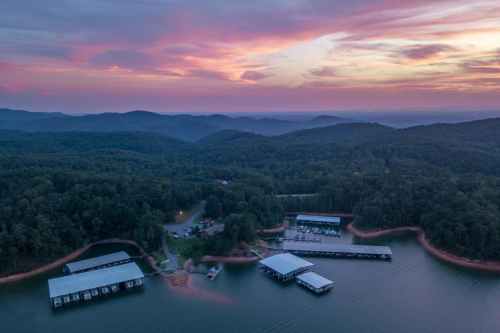 Aerial view of a serene lake surrounded by mountains at sunset, with docks and boats along the shoreline.