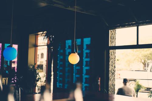 A cozy interior with colorful pendant lights and large windows, showcasing plants and a view of the outside.
