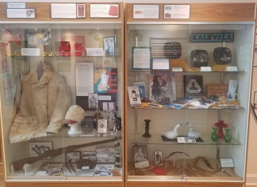 Display case featuring historical artifacts, documents, and photographs related to Finnish culture and history.