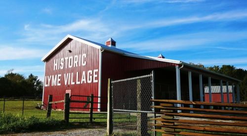 Red barn with "HISTORIC LYME VILLAGE" painted on the side, surrounded by green fields and a blue sky.
