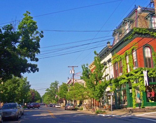 A charming street lined with historic buildings, trees, and parked cars under a clear blue sky.