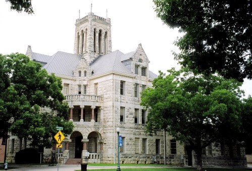 Historic stone building with a tall tower, surrounded by trees and a street sign in the foreground.