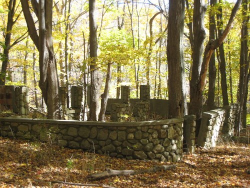 Ruins of a stone structure surrounded by trees with autumn foliage in a forest setting.