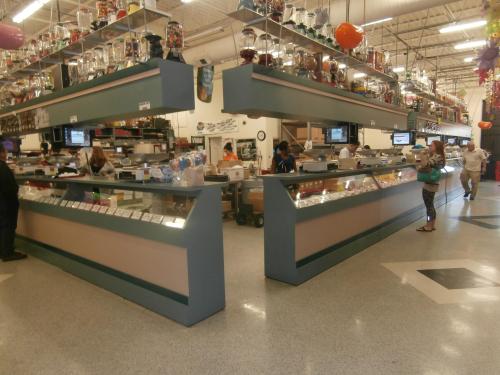 A colorful candy store interior with glass displays, customers browsing, and jars of candy overhead.