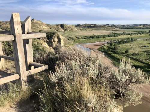 A scenic view from a cliff overlooking a winding river and lush green landscape under a clear blue sky.