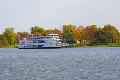 A large riverboat with a red and white design docked near a tree-lined shore in autumn.