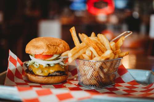 A juicy cheeseburger with lettuce and tomato, served with a side of crispy fries in a metal basket.