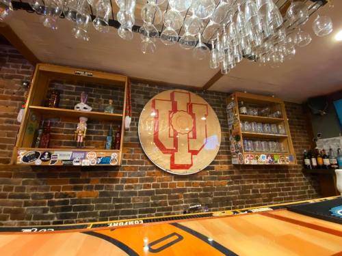 A bar interior featuring a brick wall, shelves with decor, and a large circular logo on display.