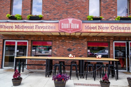Exterior of the Court Room restaurant, featuring a sign and outdoor seating with potted plants.
