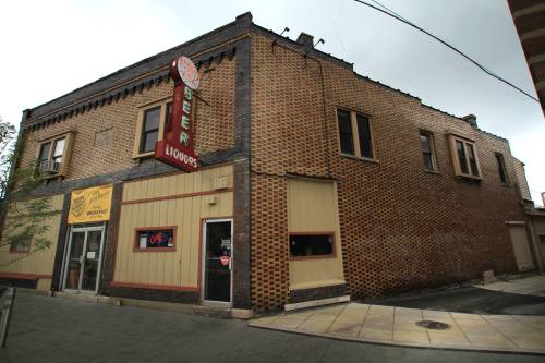 A brick building with a liquor store sign, featuring a corner entrance and large windows, set against a cloudy sky.