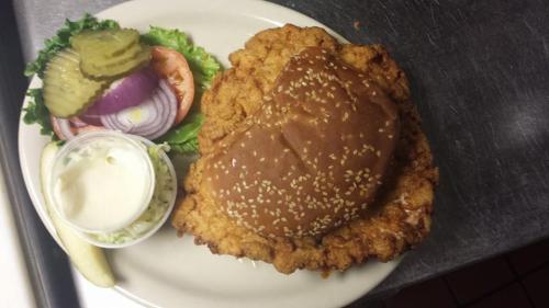A large fried chicken sandwich on a sesame seed bun, served with pickles, lettuce, onion, and a side of coleslaw.
